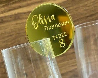 May include: Gold round acrylic table number with the name Olivia Thompson and the text "Table 8" on it.