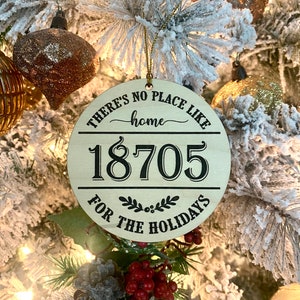 May include: A round wooden Christmas ornament with the text "There's no place like home" and the number "18705" in black lettering. The ornament also has the text "For the Holidays" in black lettering.