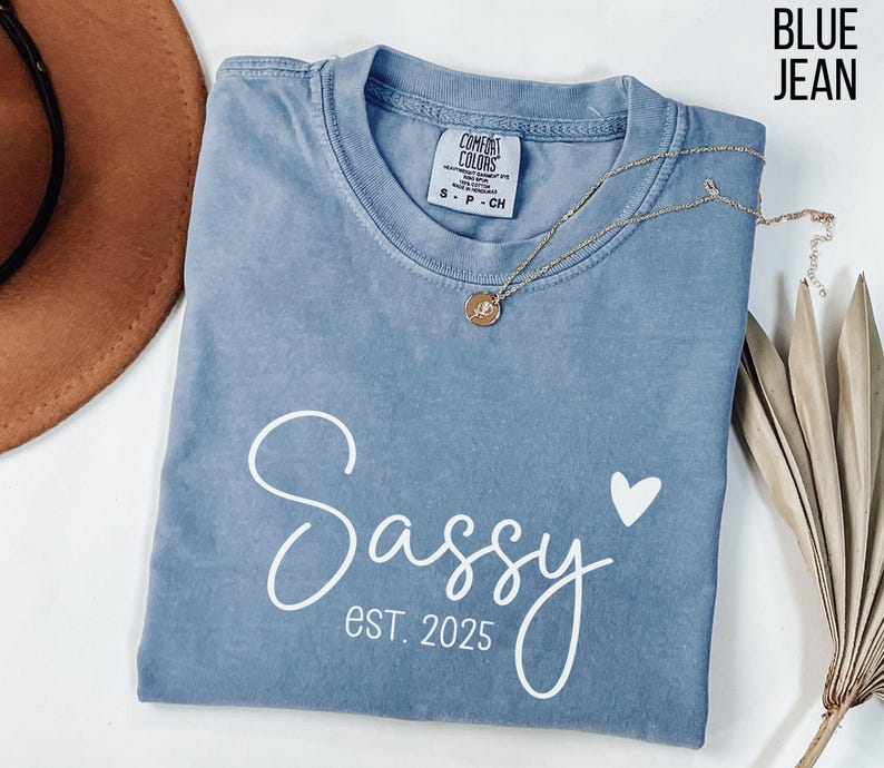 May include: A blue jean coloured t-shirt with the text "Sassy est. 2025" and a small white heart.