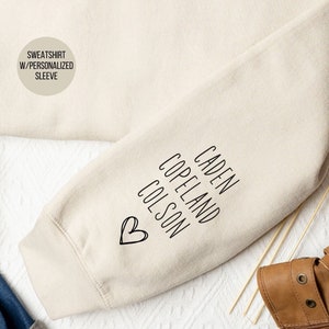 May include: A beige sweatshirt with a personalized sleeve featuring the names "Caden Copeland Colson" and a heart.
