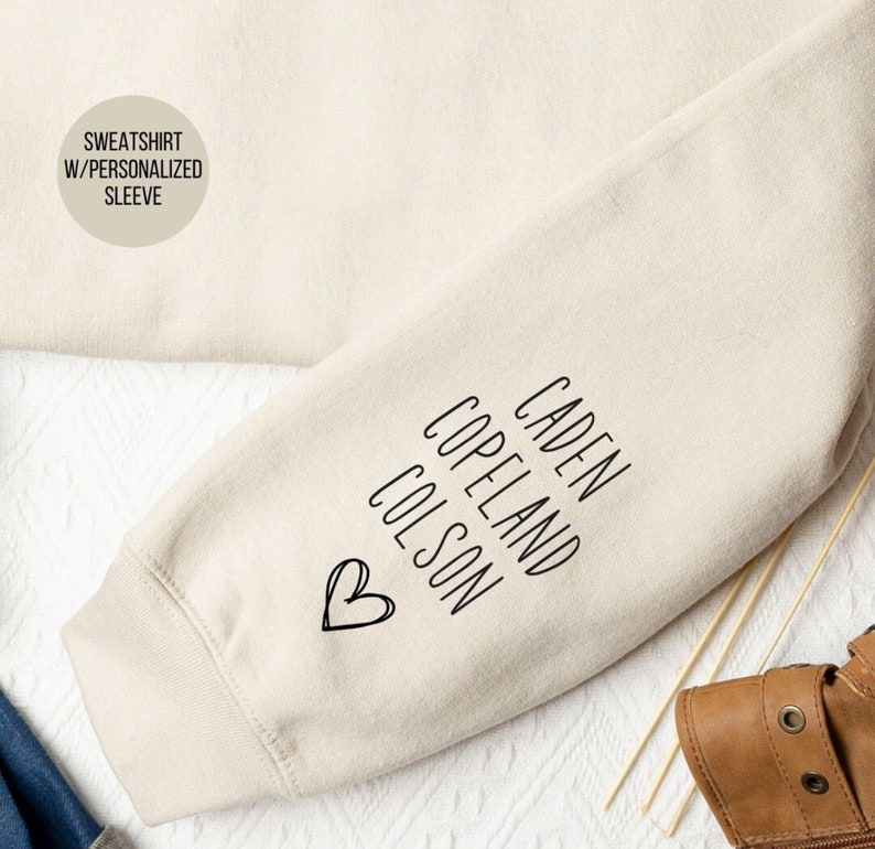 May include: A beige sweatshirt with a personalized sleeve featuring the names "Caden Copeland Colson" and a heart.