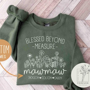 May include: An olive green sweatshirt with white text and floral design. The text reads "Blessed Beyond -Measure-" above "mawmaw" and three names. A circular logo with floral design is on the bottom right. The sweatshirt is a custom item.
