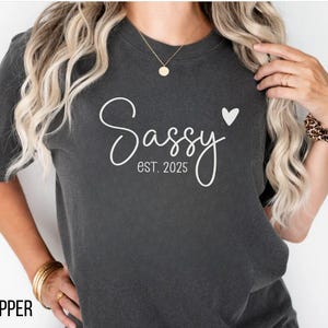 May include: A dark grey t-shirt with the text "Sassy est. 2025" and a small white heart.