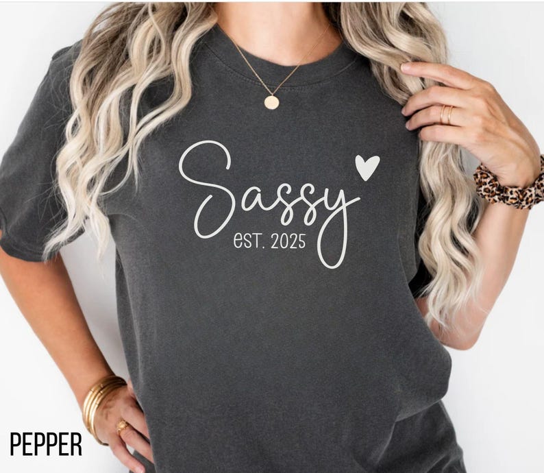 May include: A dark grey t-shirt with the text "Sassy est. 2025" and a small white heart.