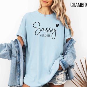 May include: A light blue t-shirt with the text "Sassy est. 2025" and a small black heart.