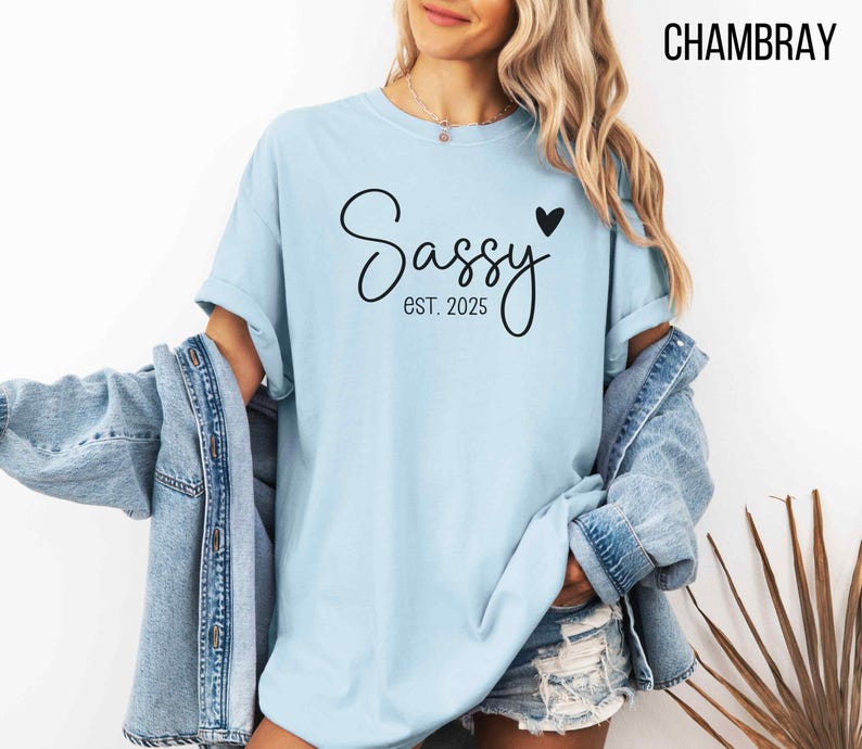 May include: A light blue t-shirt with the text "Sassy est. 2025" and a small black heart.