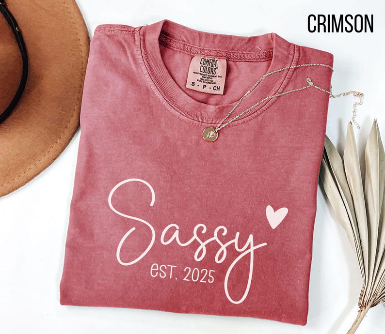 May include: A crimson red t-shirt with the text "Sassy est 2025" in white script with a small pink heart.