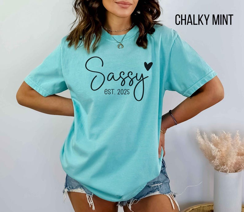May include: A turquoise blue t-shirt with the text "Sassy est. 2025" and a small black heart.