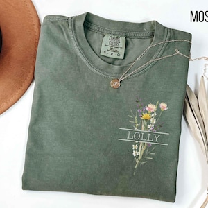 May include: A moss green t-shirt with a floral design and the word "LOLLY" printed on the front.