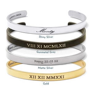 May include: Four different bracelets with various engravings. The top bracelet is silver and engraved with the word "Monty". The second bracelet is gunmetal grey and engraved with "VIII XI MCMLXII". The third bracelet is matte silver and engraved with "Poppy 22.09.22". The bottom bracelet is gold and engraved with "XII XII MMXXI".