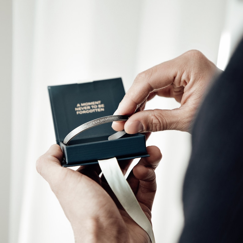 May include: A silver bracelet with the inscription "A moment never to be forgotten" in a dark blue box with a white ribbon.