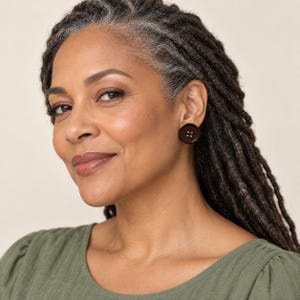 May include: A dark brown circular stud earring shaped like a four-hole button. The earring features a smooth, matte finish with four small, evenly spaced indentations in the center, mimicking the appearance of a standard sewing button.