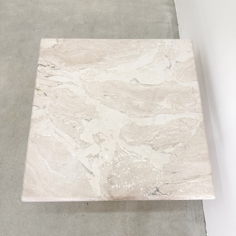May include: A square, light beige marble coffee table with a swirling pattern of darker beige and white veins.