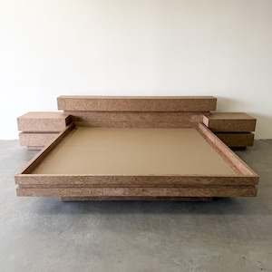 May include: A low-profile platform bed frame featuring a light brown wood grain finish with a swirling pattern. The structure includes an integrated headboard and two attached side tables, each with two drawers, creating a unified, wide furniture unit.