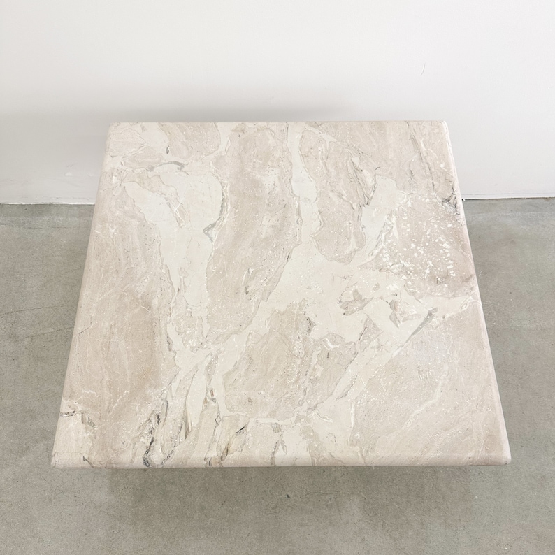 May include: A square, light beige marble coffee table with a swirling pattern.