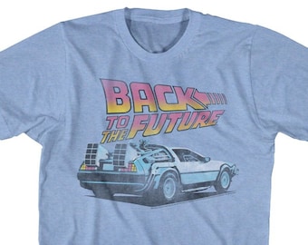 Könnte beinhalten: Ein hellblaues T-Shirt mit einem verblassten Grafikdruck des DeLorean-Zeitfahrzeugs aus dem Film "Zurück in die Zukunft". Der Text "Zurück in die Zukunft" ist in einer Retro-Schriftart mit rosa, orange und gelben Farben gedruckt.