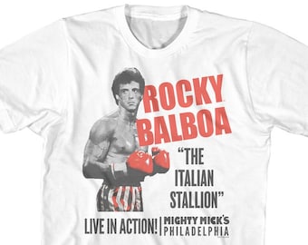 May include: White t-shirt with a red and black image of Rocky Balboa, a boxer, with the text "Rocky Balboa" and "The Italian Stallion" in red. The text "Live in Action! Mighty Mick's Philadelphia" is also printed on the shirt.