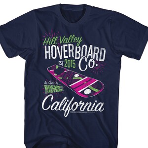 May include: A navy blue t-shirt with a white graphic of a hoverboard and the text "Hill Valley Hoverboard Co. Est 2015 California" with green and pink accents. The graphic also includes the text "As Seen In... Back to the Future."