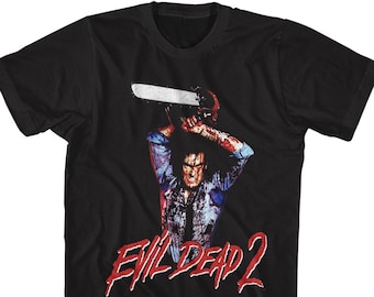 Könnte beinhalten: Schwarzes T-Shirt mit einem Grafikdruck eines Mannes, der eine Kettensäge hält, und dem Text "Evil Dead 2" in Rot.