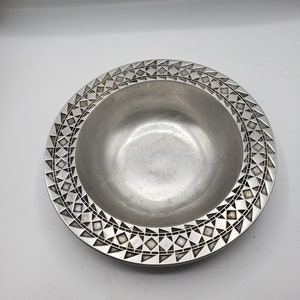 May include: A silver bowl with a geometric pattern around the rim.