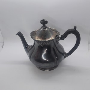May include: A silver teapot with a black handle and ornate details. The teapot has a round body and a lid with a finial.