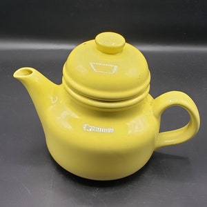 May include: A yellow ceramic teapot with a lid. The teapot has a rounded body and a spout on the side. The lid has a knob on top.