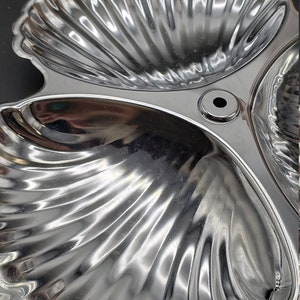 May include: A silver three-section serving dish shaped like a seashell. The dish is made of metal and has a shiny finish.
