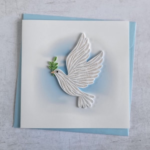 Könnte beinhalten: Handgefertigte Grußkarte mit einer weißen Taube mit ausgebreiteten Flügeln, die einen grünen Olivenzweig hält. Die Taube ist aus Papier-Quilling gefertigt und befindet sich auf einem weißen Hintergrund mit einem hellblauen Umschlag.