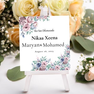 May include: A white sign with a floral border and the text "Ku Soo Dhawaada"  "Nikah Xeena" "Maryan & Mohamed" "August 26, 2023".