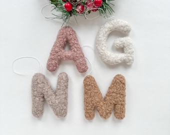 May include: Five fluffy felt letters, A, G, N, M, and a smaller A, in shades of pink, white, beige, and brown, with white string loops for hanging.