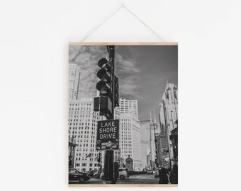 May include: Black and white photograph of a city street with tall buildings, a traffic light, and a sign that reads "Lake Shore Drive".
