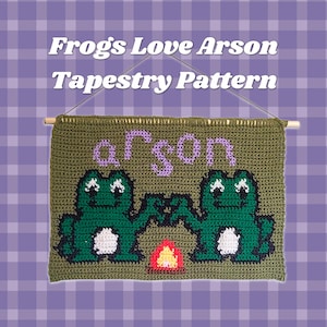May include: A rectangular olive green crochet tapestry hanging from a wooden dowel with a string. The design features two dark green frogs with white bellies, a small orange and yellow campfire, and the purple text "arson" above the frogs.