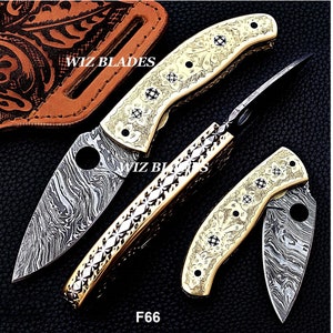 May include: Three folding pocket knives with Damascus steel blades and gold-colored handles. The handles are decorated with floral patterns. The knives are open and closed, showing the blades and the handles. The text "WIZ BLADES" and "F66" are visible on the image.