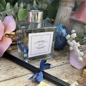 Könnte beinhalten: Ein klarer Glasflaschen-Rieddiffusor mit silbernem Verschluss. Die Flasche enthält blauen und goldenen Glitzer. Das Etikett lautet "Lapis Lazuli Reed Diffuser".