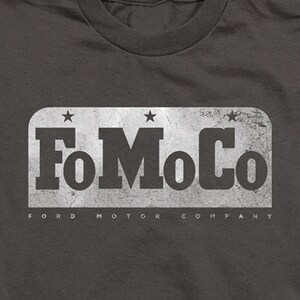 May include: A dark grey t-shirt with a white vintage-style logo that says "FoMoCo Ford Motor Company" with three stars above the text.