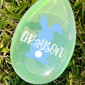 May include: A clear plastic Easter egg with a blue bunny and the name Grayson written in white.