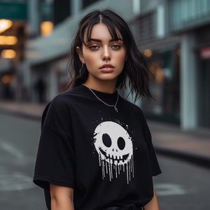 May include: A black t-shirt featuring a white graphic of a dripping skull face. The skull is smiling and has a white outline.