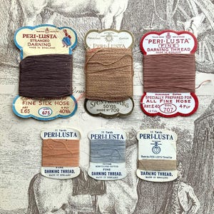 Op de afbeelding: Een assortiment vintage Peri-Lusta stopgaren spoelen in verschillende kleuren, waaronder bruin, beige en perzik. De spoelen hebben decoratieve labels met tekst en illustraties, en zijn gerangschikt op een patroonachtergrond.