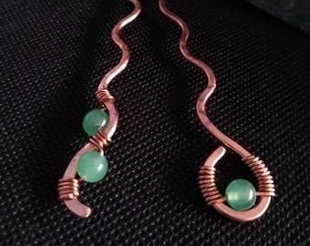 May include: Two copper hair pins with a wavy design. Each pin has a green gemstone wrapped in copper wire.