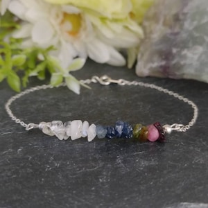 May include: A silver chain bracelet featuring a row of colourful gemstone chips. The stones are clear, blue, green, pink, and red.