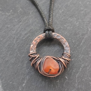 May include: A copper wire wrapped carnelian gemstone pendant with a hammered copper circle and a black cord.