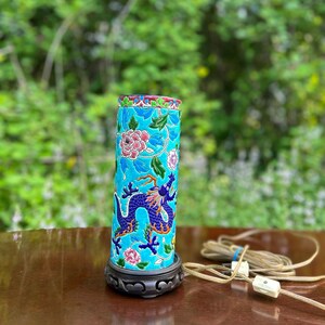 Puede incluir: Una l&aacute;mpara de mesa de cer&aacute;mica azul y verde con un dise&ntilde;o de drag&oacute;n y flores. La l&aacute;mpara tiene una base de madera y un cable con un interruptor blanco.