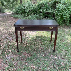 May include: A dark wood writing desk with a single drawer and brass hardware. The desk has a simple, elegant design and is perfect for a home office or study.