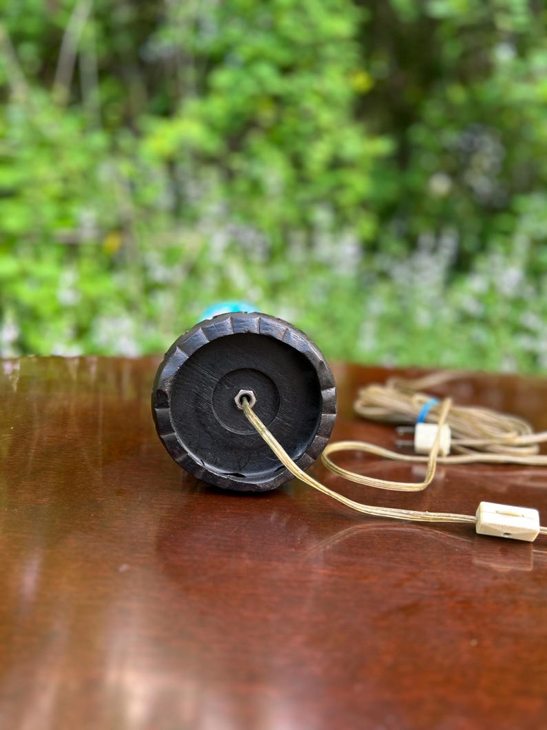 Puede incluir: La parte inferior de una base de l&aacute;mpara negra con un cable y un enchufe. La base tiene un dise&ntilde;o circular texturizado.