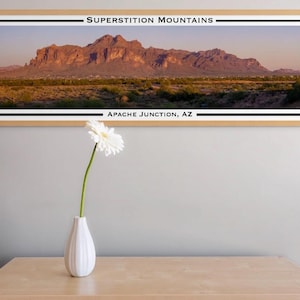 May include: A framed panoramic photograph of the Superstition Mountains in Arizona. The mountains are a reddish-brown color and are surrounded by desert vegetation. The text "Superstition Mountains" and "Apache Junction, AZ" is printed at the top and bottom of the image.