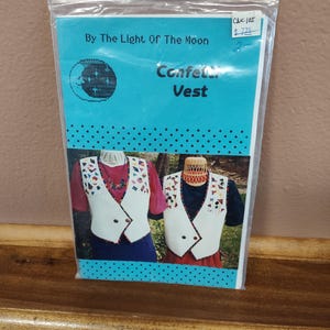 May include: A sewing pattern for a vest called "Confetti Vest" by The Light of the Moon. The pattern features two models wearing the vest, one in a red shirt and the other in a blue shirt. The pattern is priced at $7.75.
