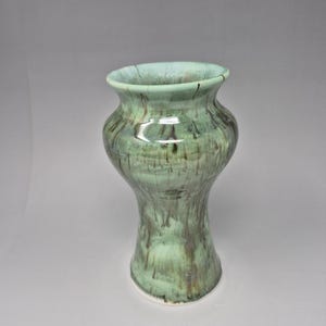May include: A handcrafted ceramic vase with a unique shape and a blend of green and brown glaze. The vase has a wide mouth and a bulbous body, standing approximately 8 inches tall.