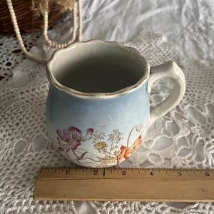 Pu&ograve; includere: Una tazza in ceramica vintage blu e bianca con un motivo floreale. La tazza ha un bordo ondulato e un manico. Misura circa 7,5 cm di altezza.