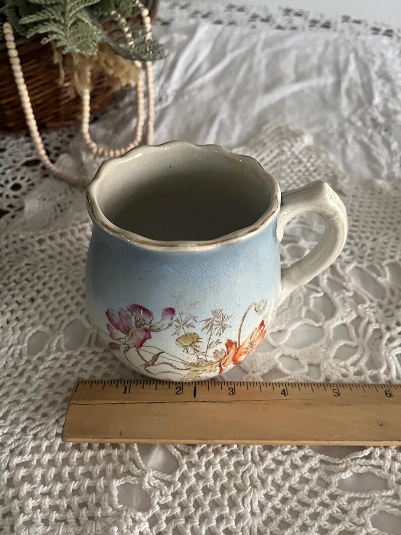 Pu&ograve; includere: Una tazza in ceramica vintage blu e bianca con un motivo floreale. La tazza ha un bordo ondulato e un manico. Misura circa 7,5 cm di altezza.