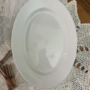 May include: A white oval serving platter with a raised rim. The platter is made of ceramic and has a smooth, glossy finish.